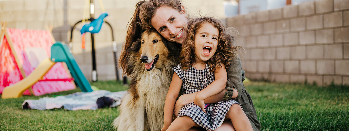 Portrait view of a smiling mother, daughter, and dog at home in their backyard